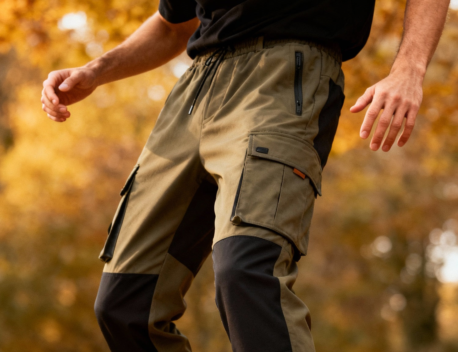Olive and black men's cargo pants with multiple pockets, set against a fall-themed outdoor background with autumn leaves.