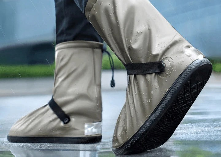 Close-up of waterproof shoe covers worn in the rain, featuring a beige waterproof fabric with black non-slip soles and adjustable straps.