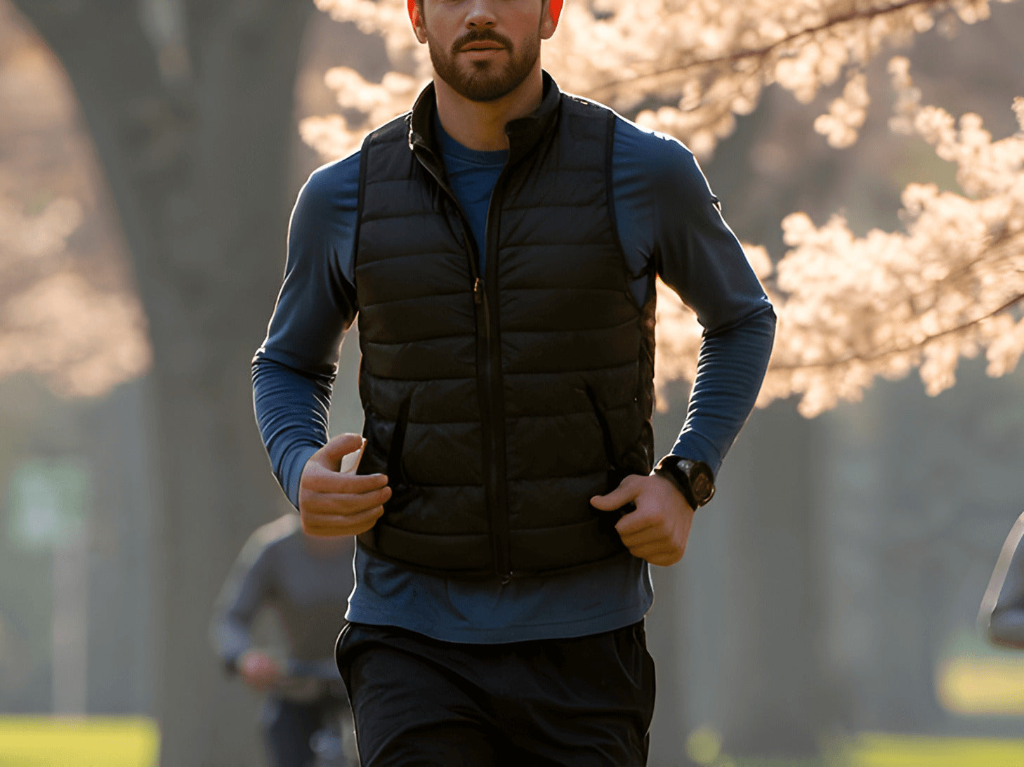 He is wearing a black, quilted puffer vest over a long-sleeve blue athletic shirt, black running pants, and a sports watch on his wrist. The lighting suggests an early morning or late afternoon run.