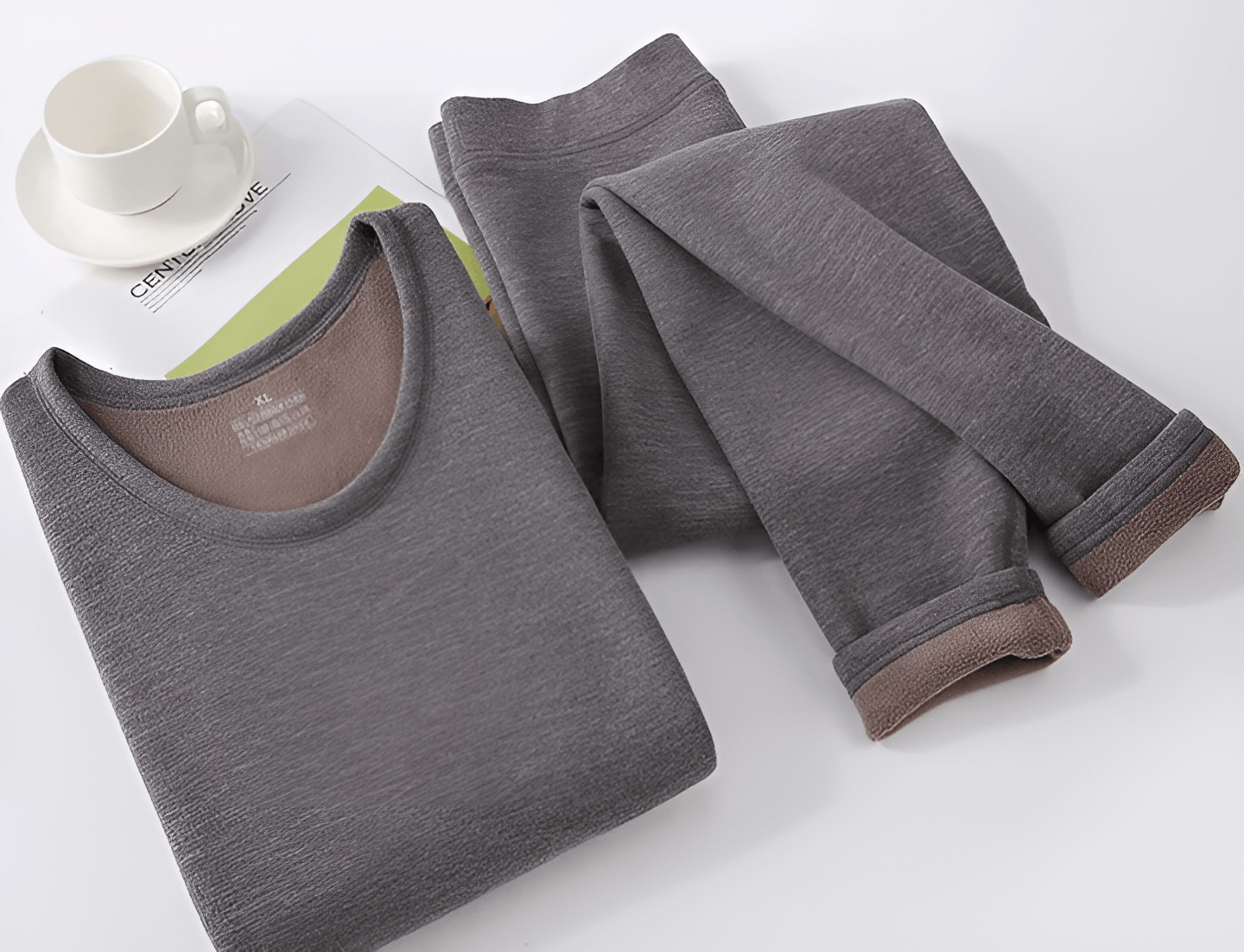 A cozy, gray thermal shirt and matching pants set laid flat on a surface, with a white cup and a magazine in the background.