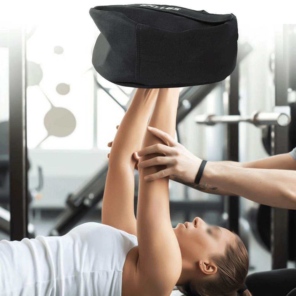 Person lifting 100 LB strongman sandbag during a workout in a gym setting.