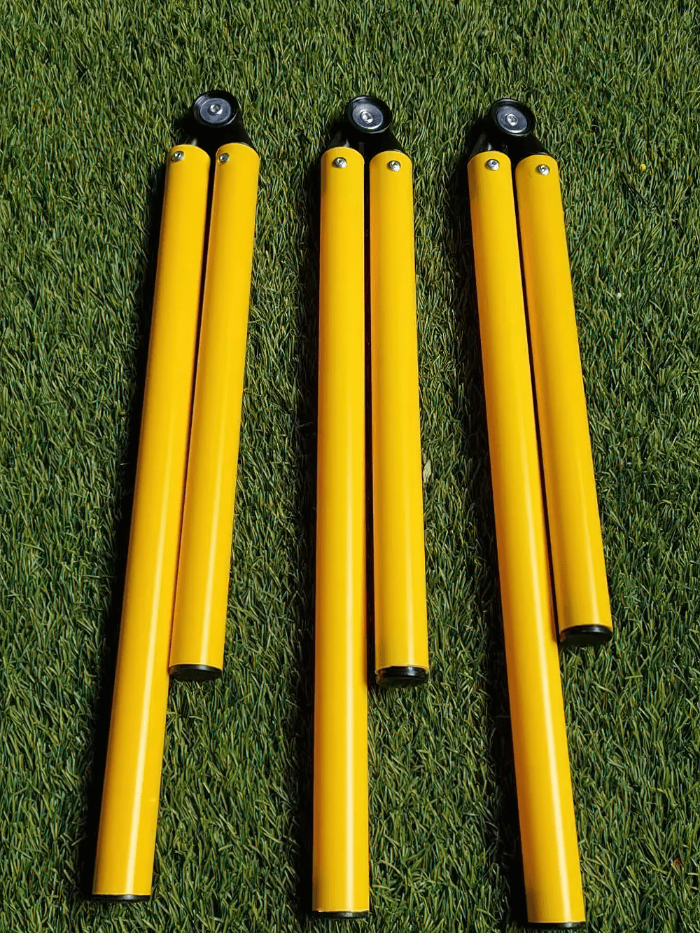 Four folded yellow adjustable agility poles on grass, ideal for soccer training and footwork drills.