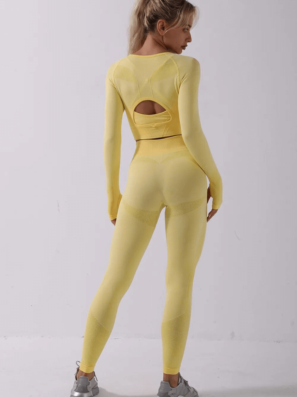 Woman wearing a yellow seamless yoga set, featuring a full-sleeve top and leggings, showcasing the back design. Perfect for sports.
