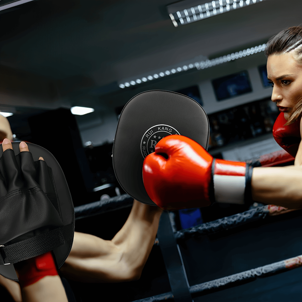 Person training with black boxing mitts and red gloves in a gym setting, showcasing focus and intensity in fitness and MMA practice.