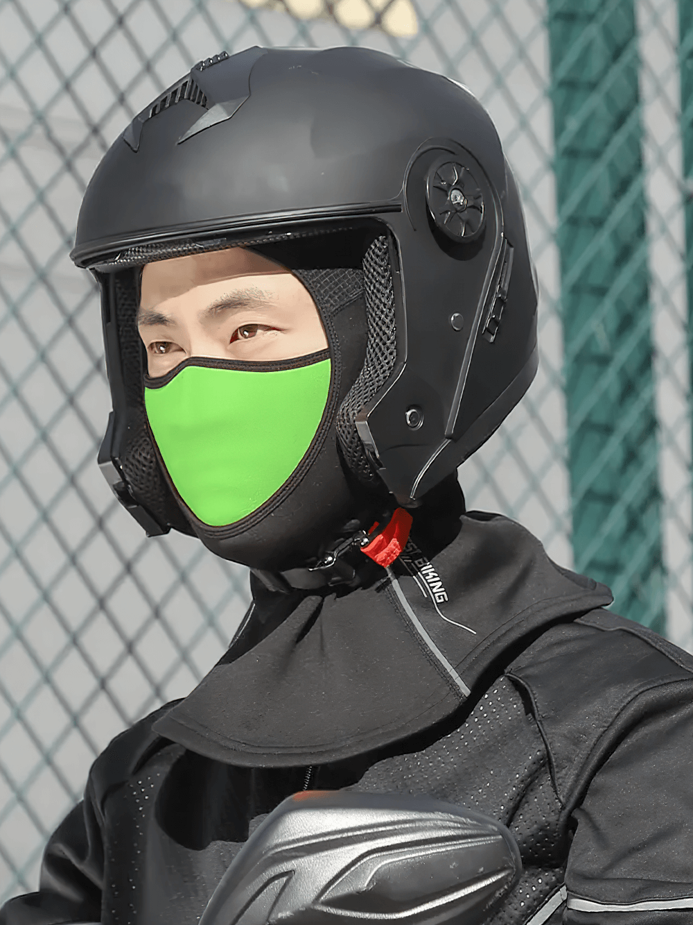 Person wearing a black helmet and 3-in-1 thermal balaclava with green face mask, ideal for winter sports and windproof protection.