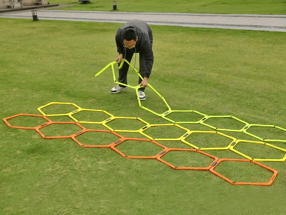 Person setting up modular hexagonal agility hurdles on grass for training. Features vibrant hex rings and speed clips for sports drills.