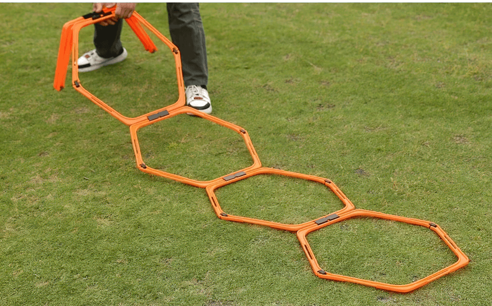 Person setting up modular hexagonal agility hurdles and connectors on grass for speed training.