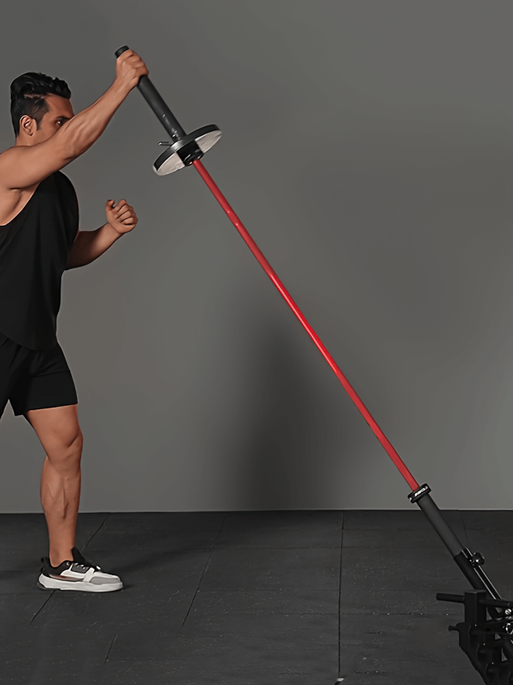 Man exercising with a red landmine barbell attachment in a gym setup.