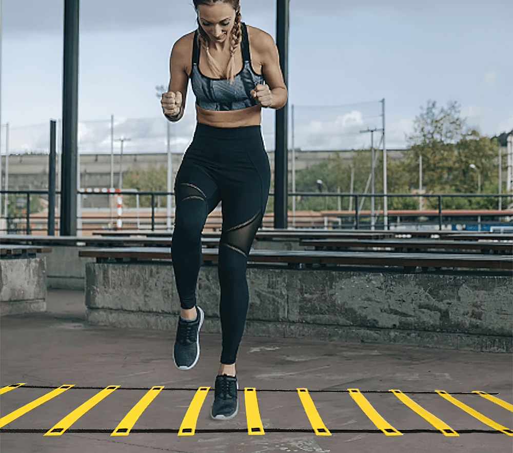 Woman performing speed drills on adjustable agility ladder outdoors.