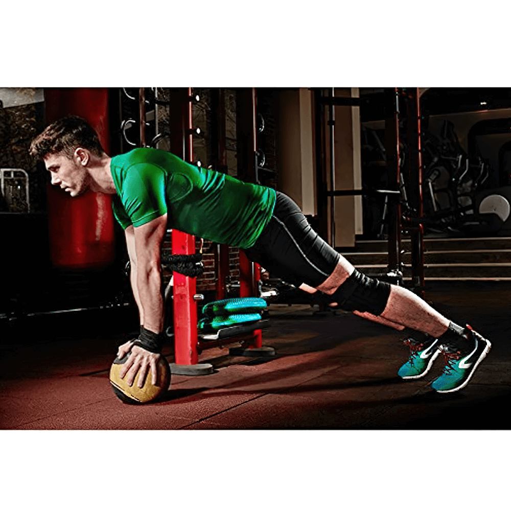 Man in green shirt doing plank on medicine ball, wearing gym wrist support brace, SF3158, in a fitness center.