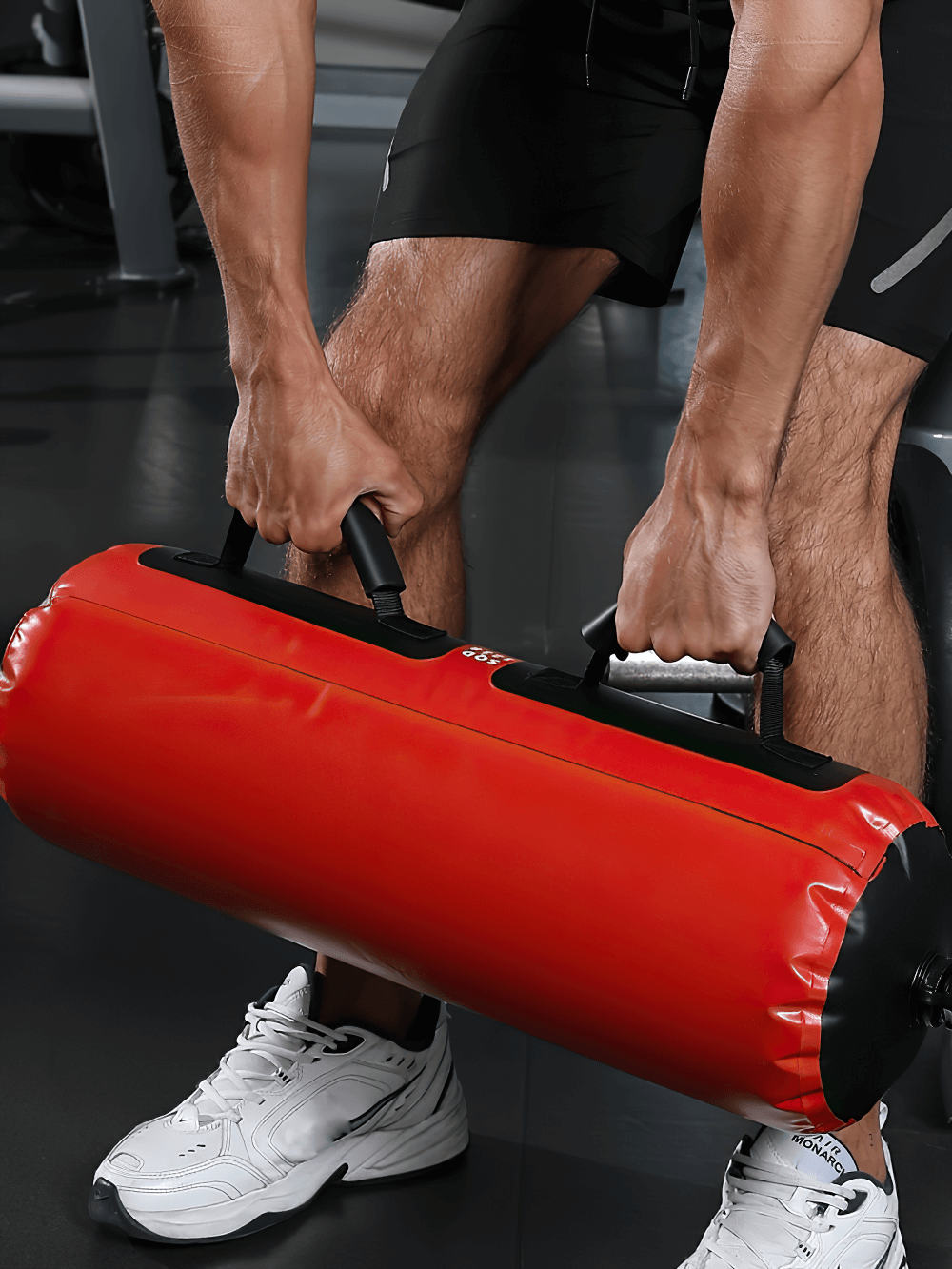 Person lifting a red adjustable weighted sandbag with reinforced handles in a gym setting, ideal for functional fitness workouts.