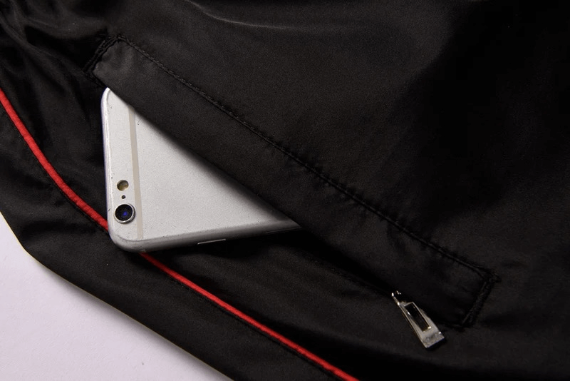 Close-up of tracksuit pocket with zipper detail, displaying secure phone storage. Athletic pants with red stripe accent.