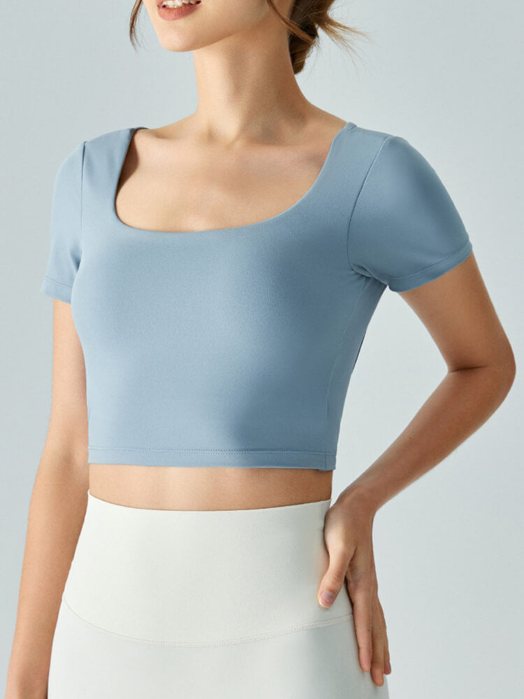 Woman wearing a light blue hollow back yoga t-shirt with short sleeves, showcasing a stylish sports crop top, perfect for workouts.