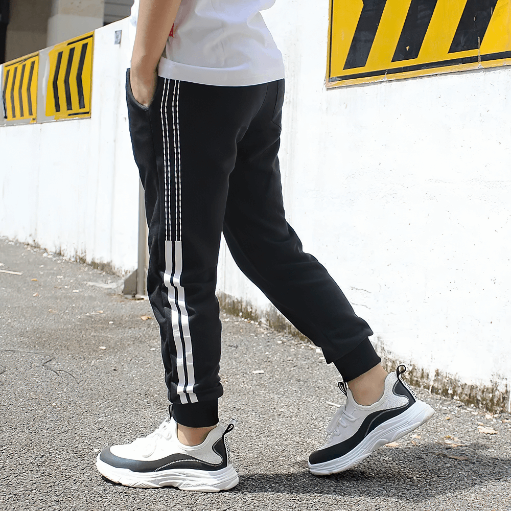 Side view of black Boys Athletic Jogger Sweatpants with Pockets - SF3611, featuring stripe details and worn with sneakers.
