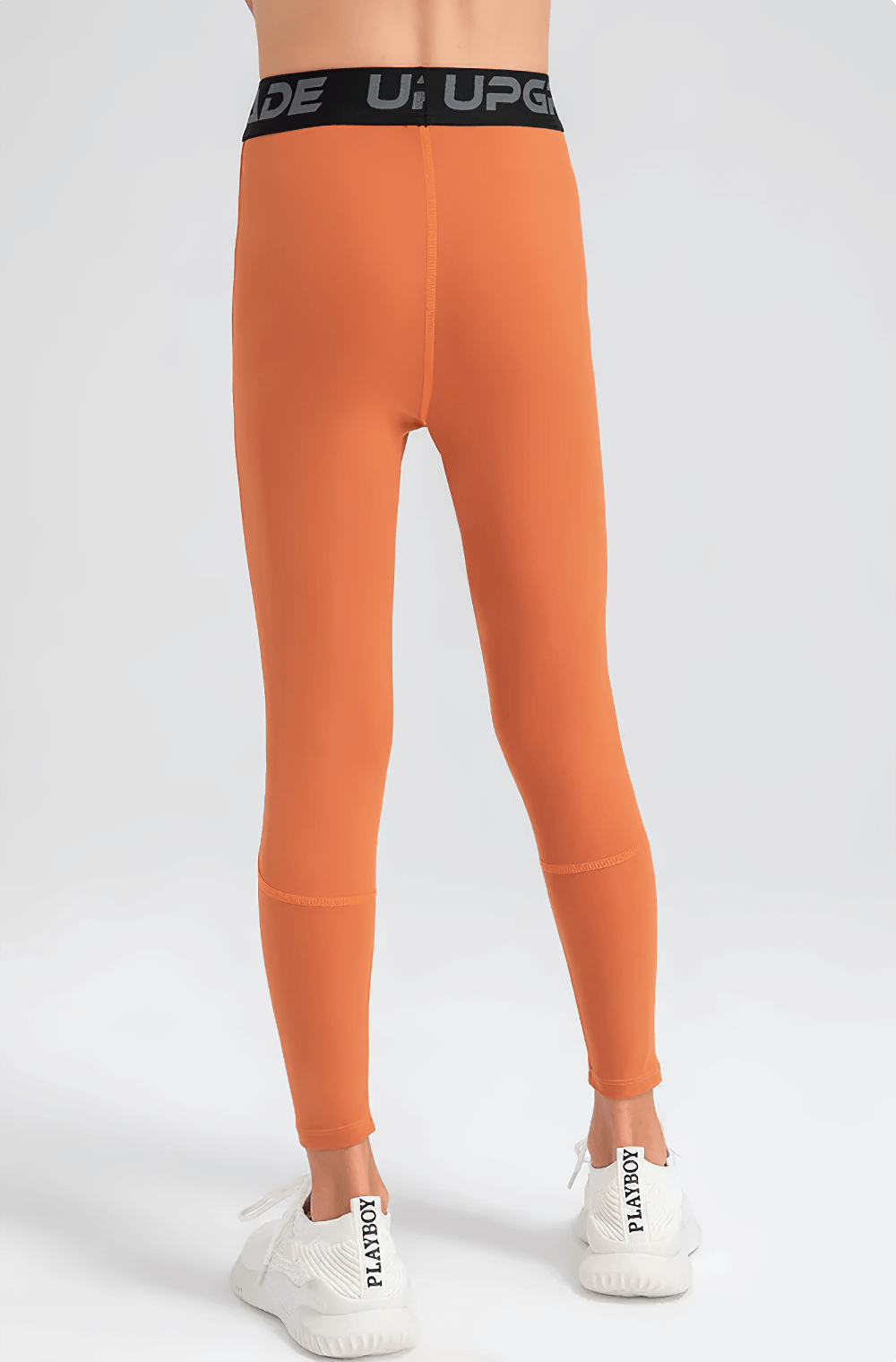 Back view of Boys Elastic High-Waisted Fitness Leggings - SF3780 in orange with black waistband over white sneakers.