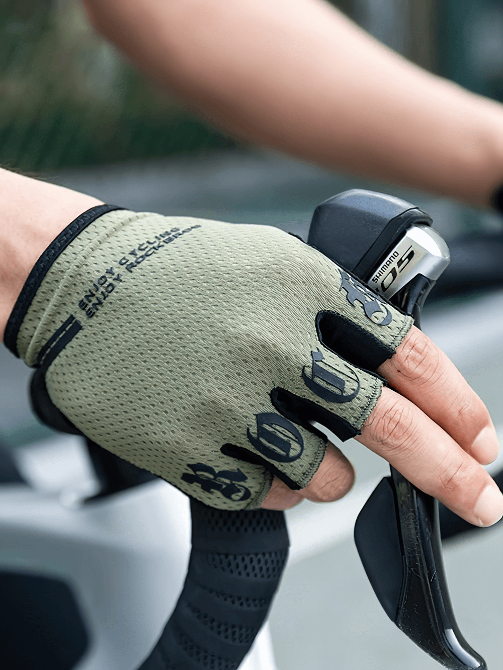 Cyclist wearing green half-finger breathable cycling gloves with anti-shock SBR pads gripping handlebars.