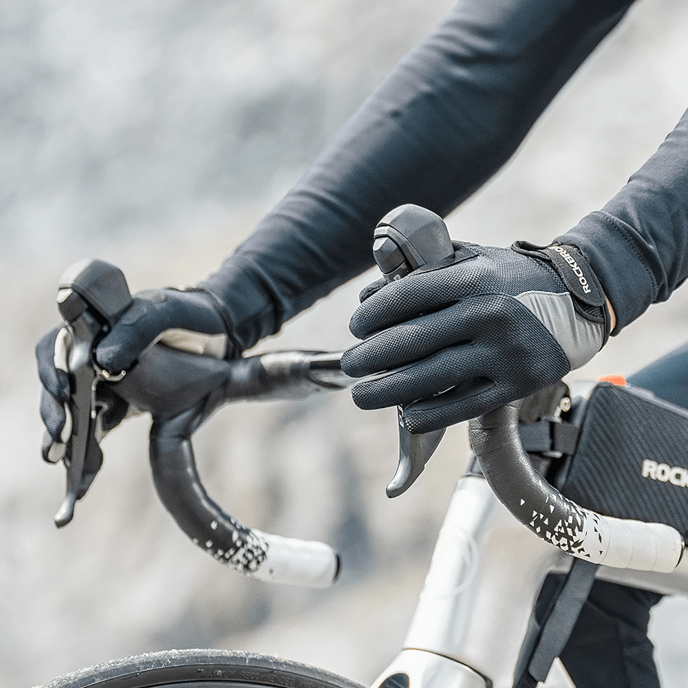 Cyclist wearing breathable windproof cycling gloves with touchscreen fingertips, gripping bike handlebars outdoors.