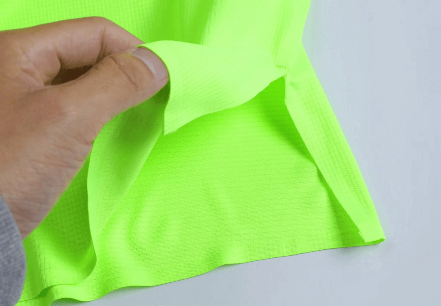Close-up of vibrant neon green fabric with perforated texture, perfect for breathable athletic wear like a men's workout tank top.