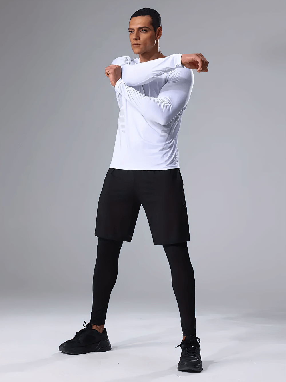 Man stretching in Breathable Men's 3-Piece Workout Set, wearing a white long-sleeve top, black shorts, and compression tights for running.