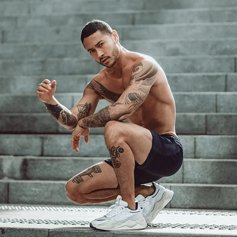Man wearing breathable black athletic shorts SF2157, showcasing tattoos while posing on steps, highlighting style and function.