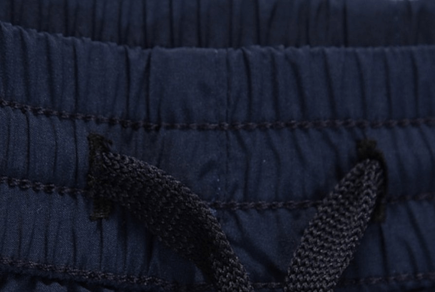 Close-up of elastic waistband with drawstring on breathable quick-dry men's shorts, navy blue color.