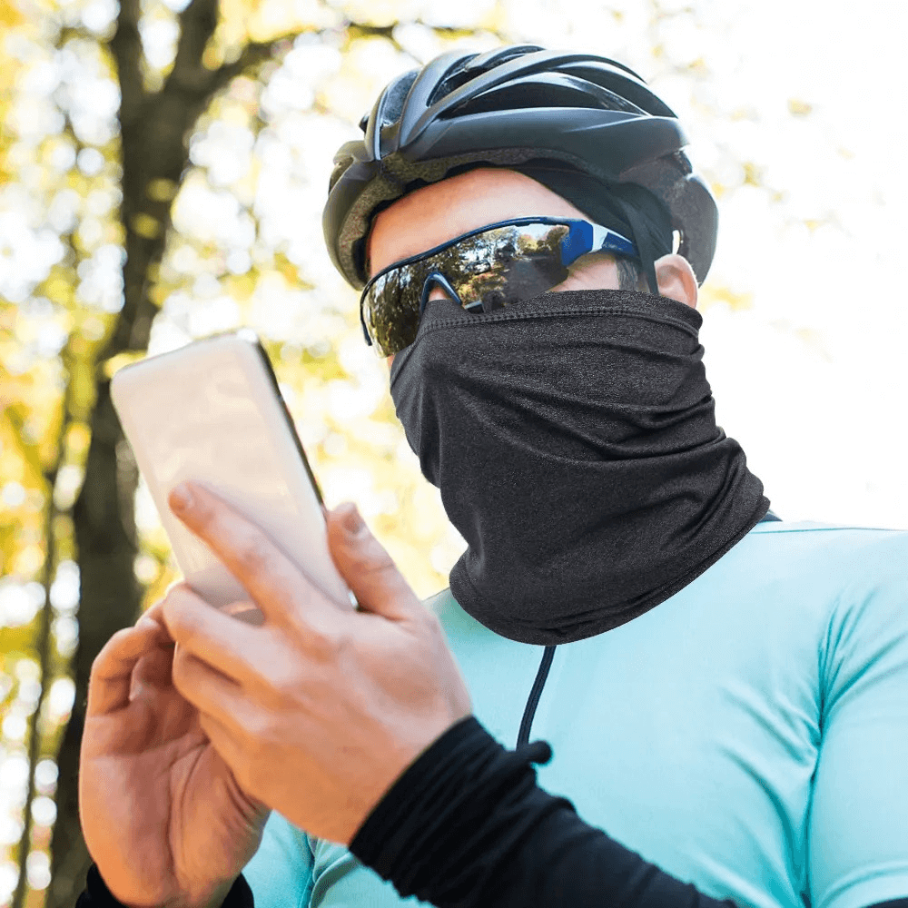 Cyclist wearing a breathable tactical neck gaiter with UV protection, checking phone while enjoying outdoor activities.