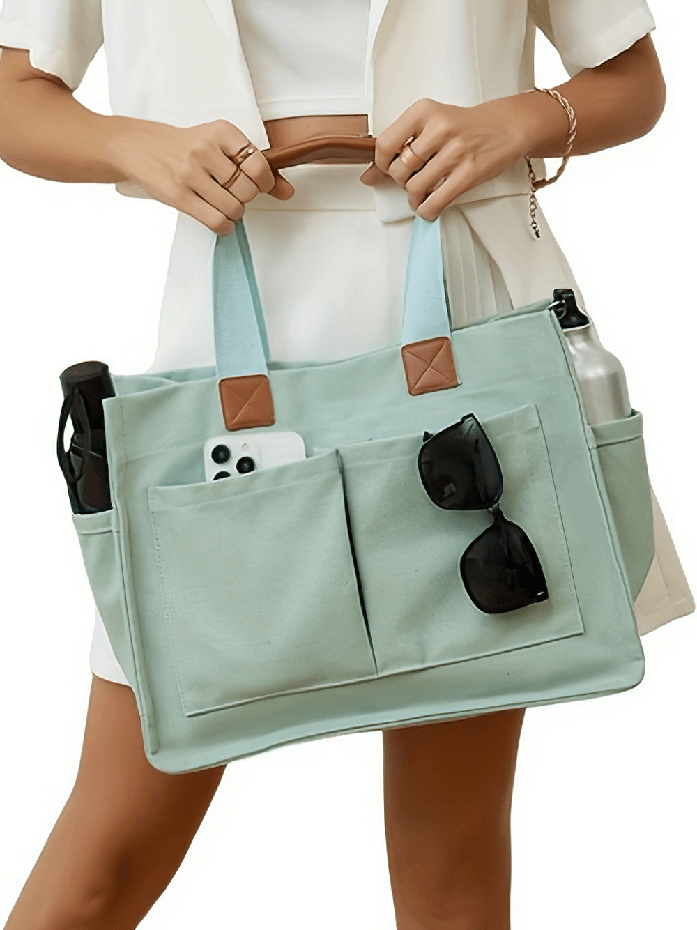 Woman carrying a mint green capacity canvas tote bag with adjustable strap, filled with phone, sunglasses, and water bottle.