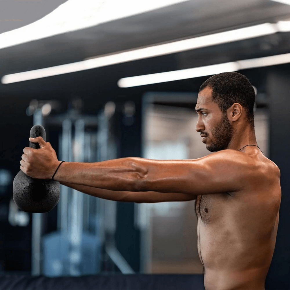 Man performing kettlebell swing with cast iron kettlebell at the gym for strength and conditioning workout.