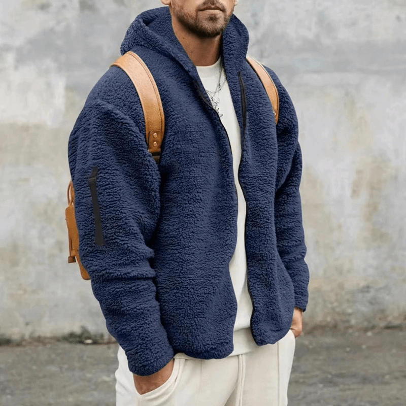 Man wearing casual fleece zip-up hooded jacket in blue with backpack, ideal for outdoor activities. Made of cotton and polyester.
