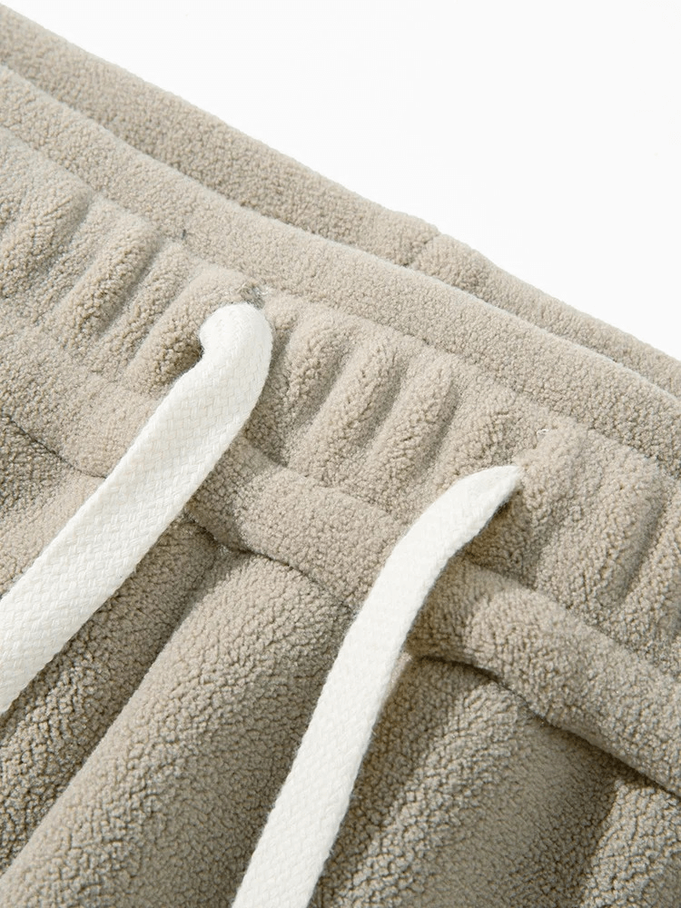 Close-up of beige fleece sweatpants with white drawstring detail, showcasing soft heavyweight fabric for warmth and comfort.