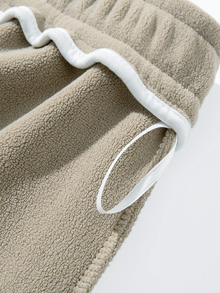 Close-up of men's wide fleece sweatpants, showcasing cozy beige fabric and white drawstring detail for added comfort and style.