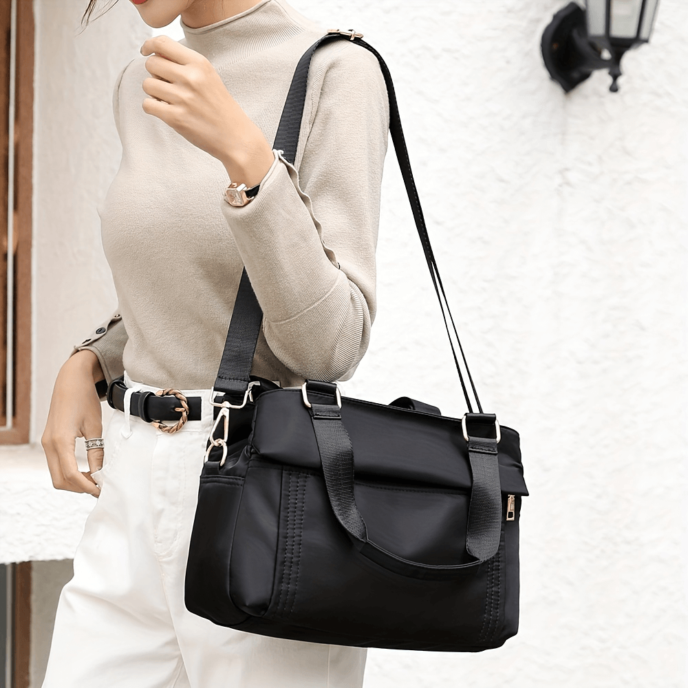 Chic multi-pocket nylon tote bag with removable strap worn by model in beige top and white pants.