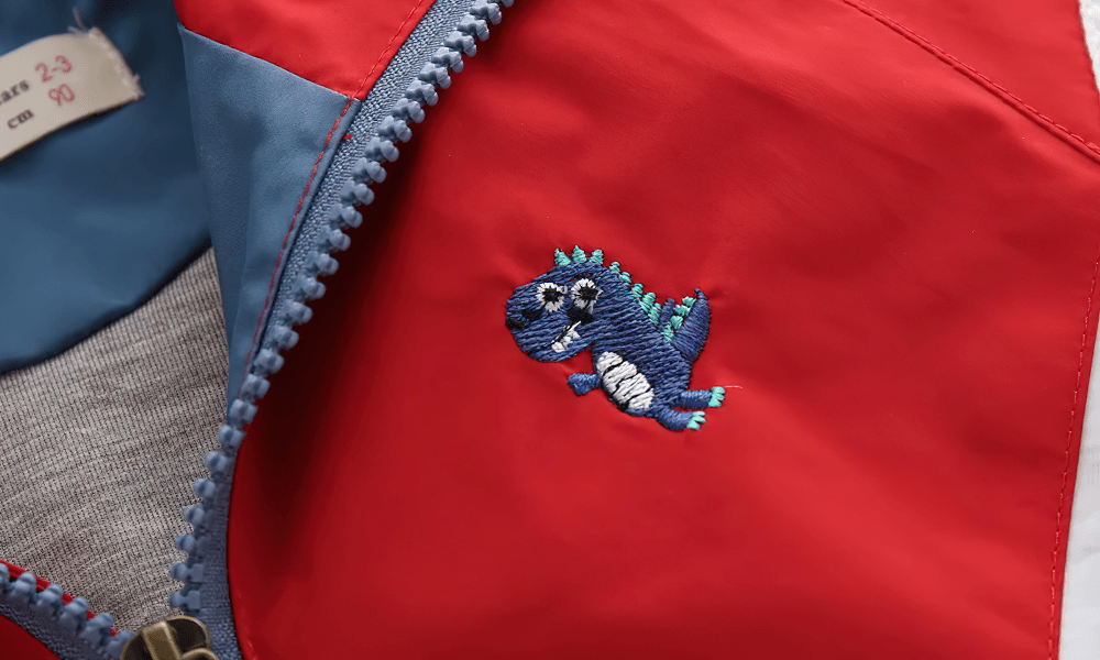 Close-up of Colorblock Hooded Windbreaker Jacket for Kids - SF3603 featuring a cute dinosaur patch on the fabric.