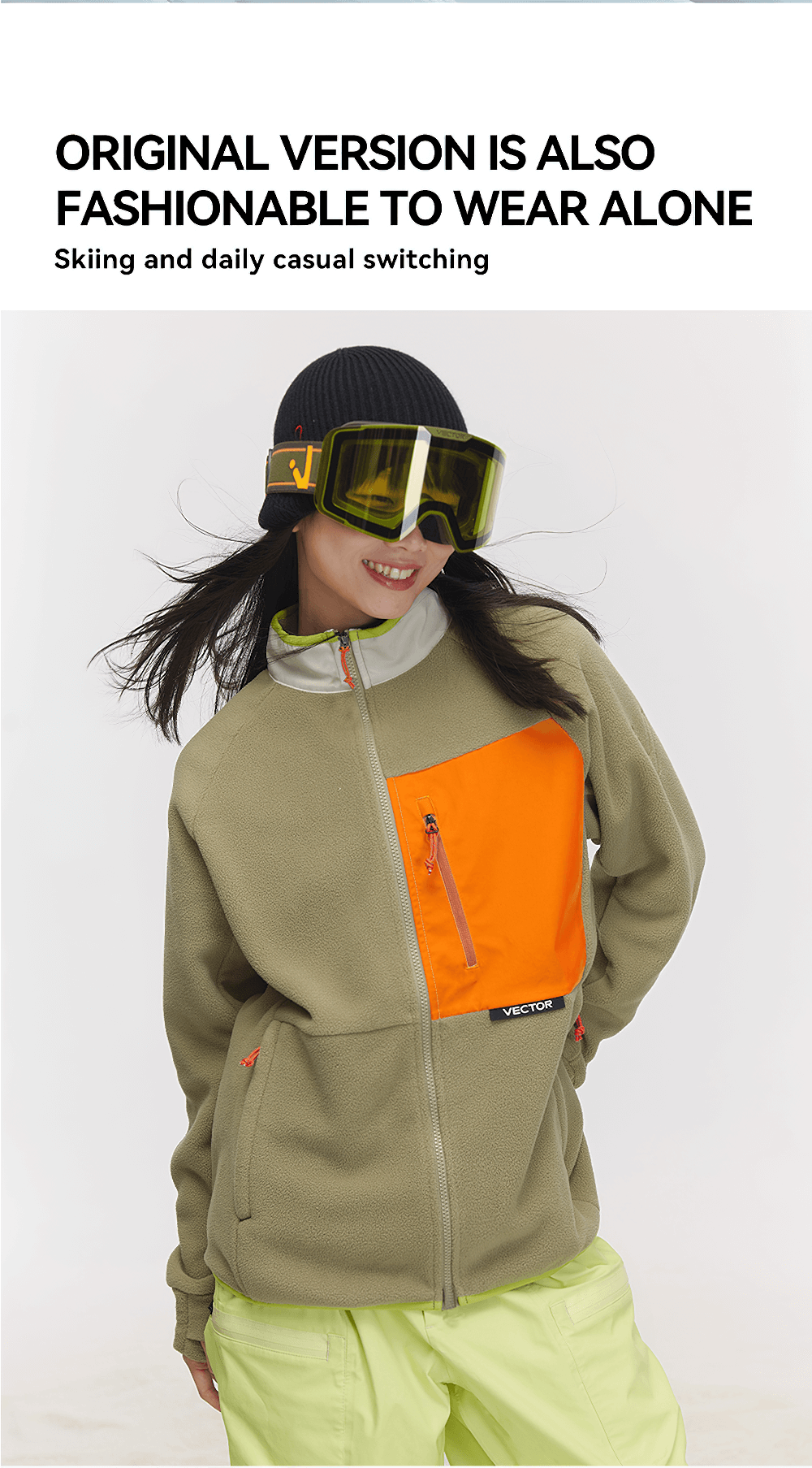 Woman wearing a contrast full-zip fleece jacket for skiing with vibrant orange pocket, smiling and posing confidently in winter gear.