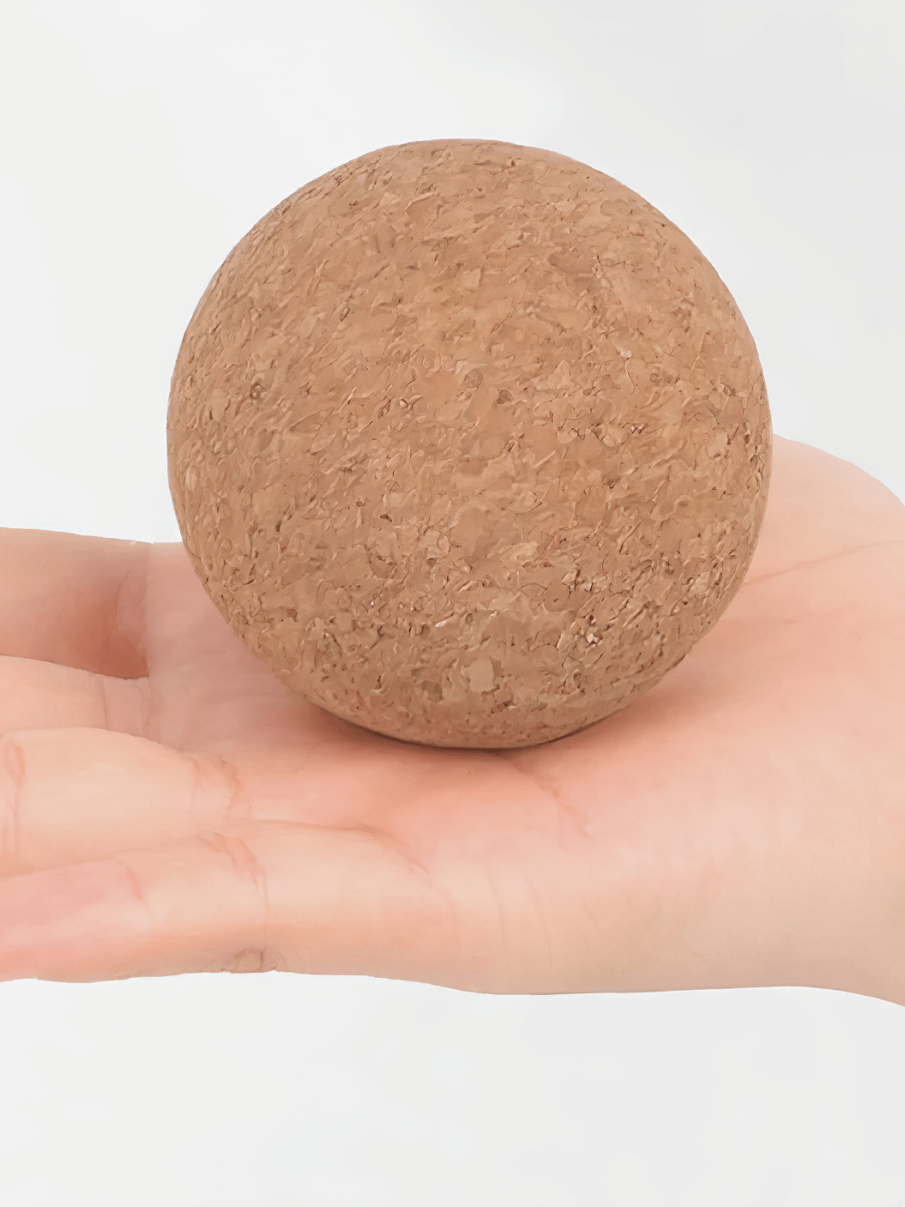 Natural cork massage ball for fascia trigger points resting on an open hand, perfect for muscle tension relief in yoga and fitness.