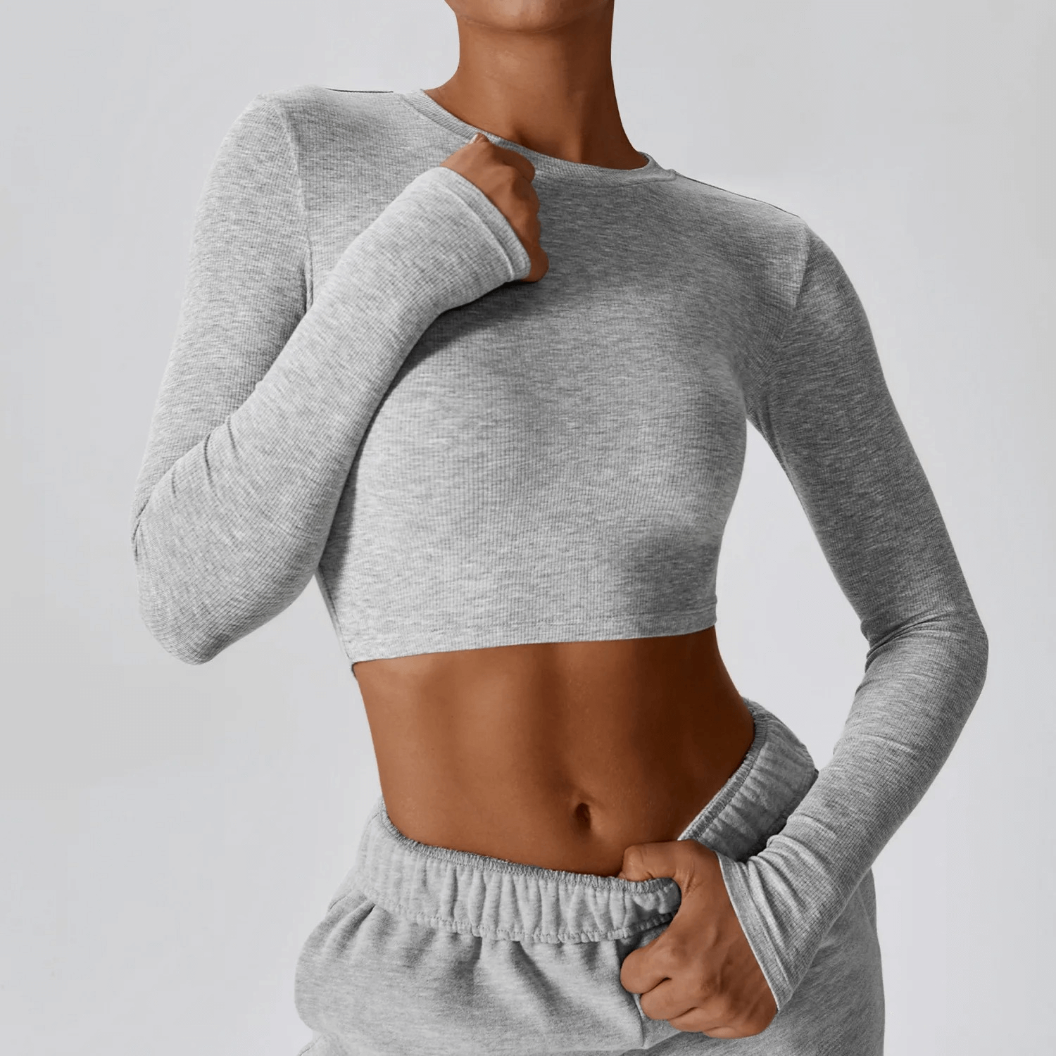 Woman wearing a grey cropped solid color long sleeves top for yoga, showcasing fashionable and breathable design with anti-pilling fabric.