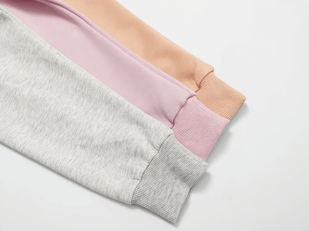 Alt Tag: Three folded sweatshirts in gray, pink, and peach with ribbed cuffs, showcasing trendy and versatile activewear fabric.