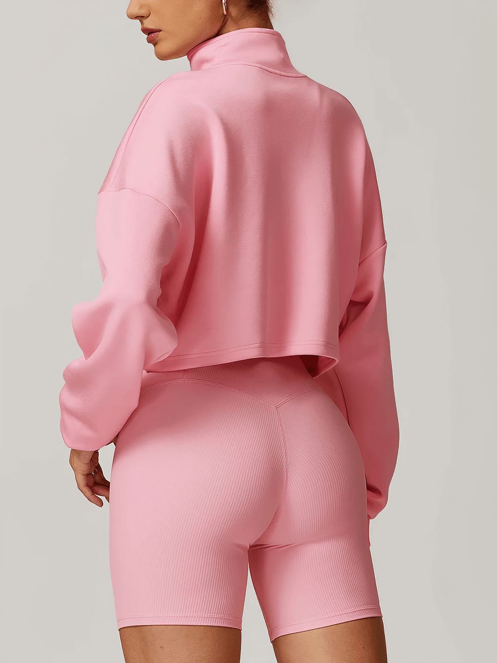 Woman wearing pink cropped zip-up loose sweatshirt and biker shorts, showing back view with relaxed fit and drop shoulder design.