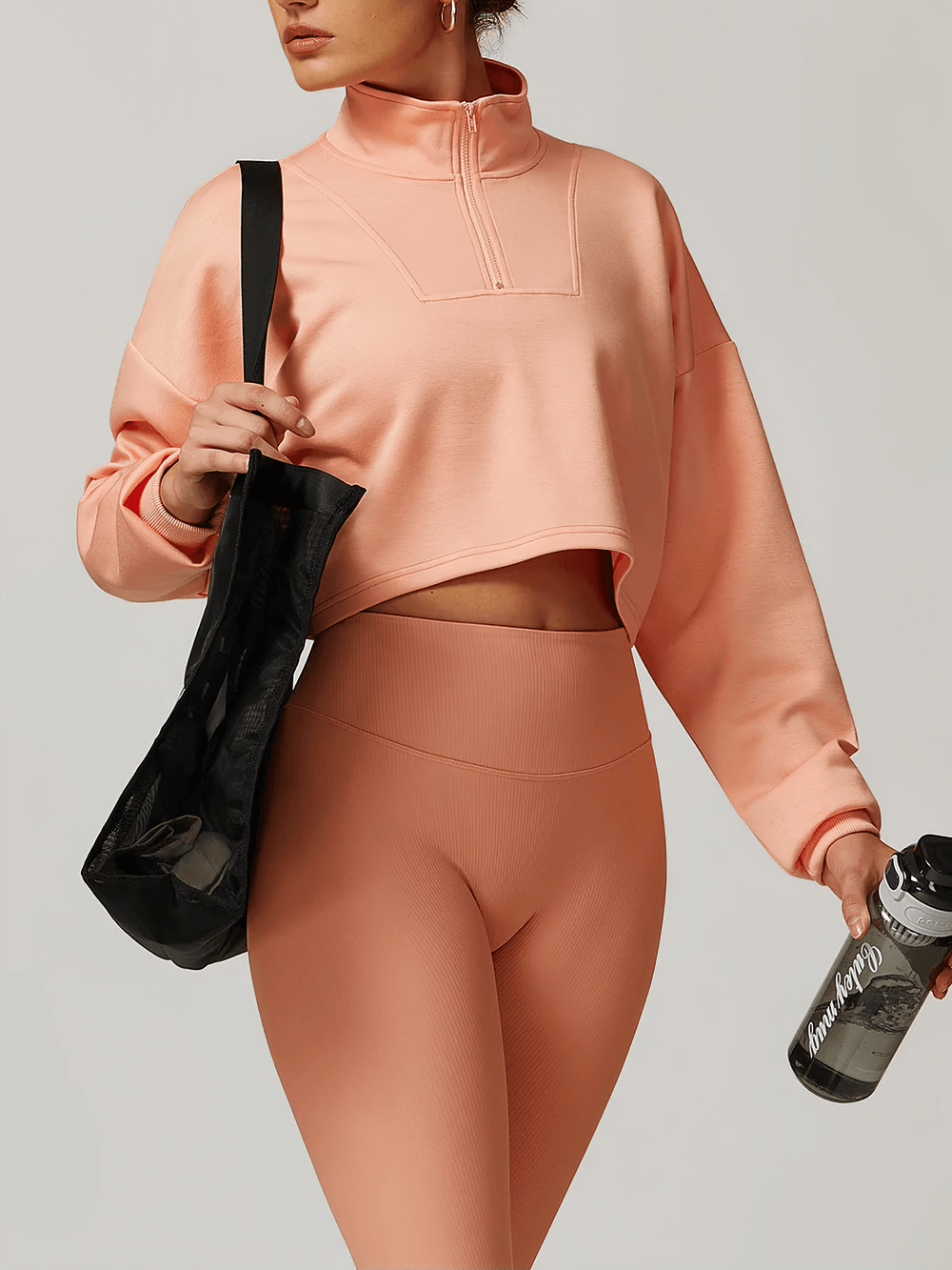 Woman wearing a trendy pink cropped zip-up sweatshirt, perfect for activewear, with a stylish half-zip and relaxed fit, holding a black bag.