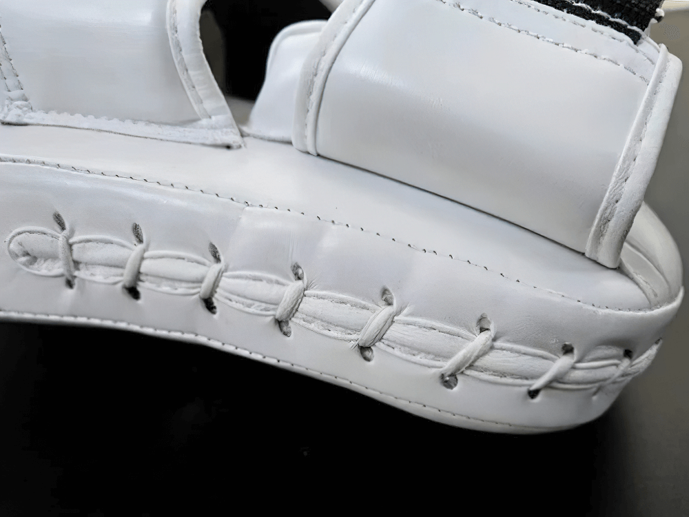 Close-up of white curved focus pads with reinforced stitching for boxing training and impact absorption.