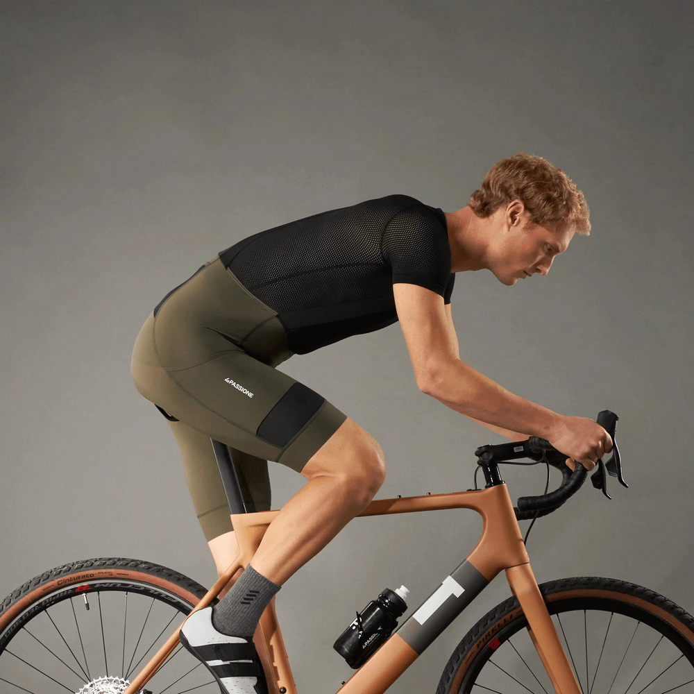 Cyclist wearing men's cycling bib shorts with 3D shockproof sponge pad, riding a bike indoors, showcasing ergonomic design and breathable fabric.