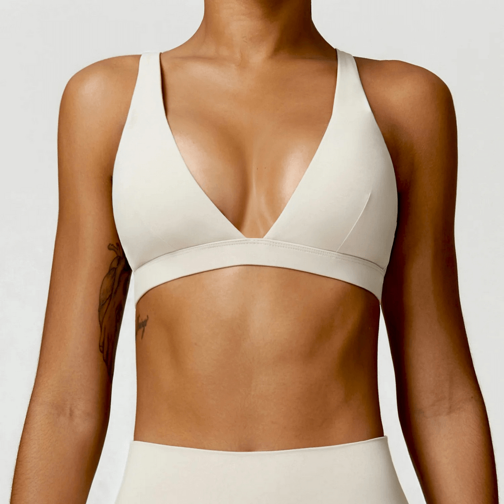 Deep V-neck padded sports bra for fitness, yoga, and running in white; shockproof design for active women. Model wearing a sleek sports bra.