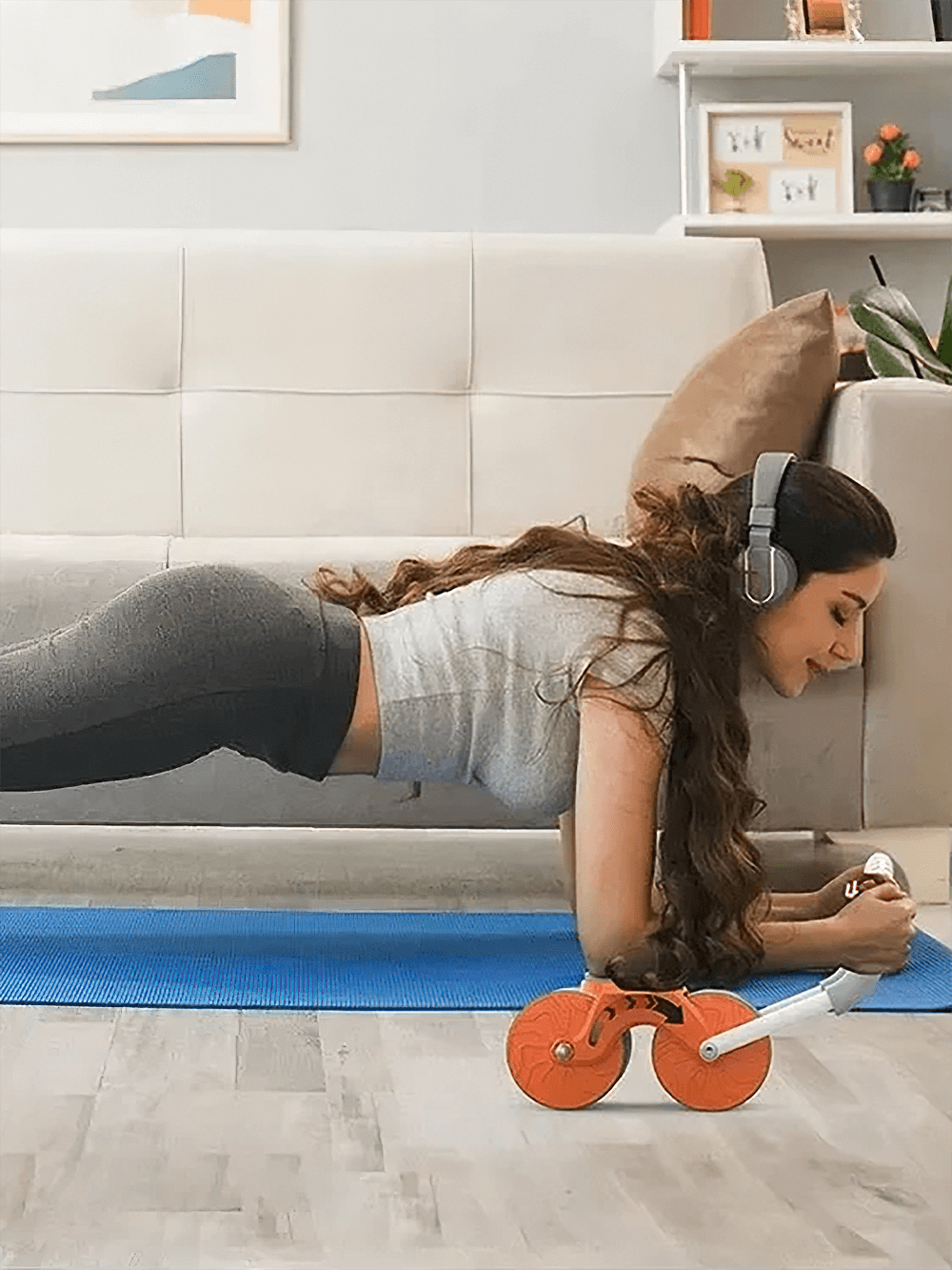 Woman using digital timed abdominal roller with knee pads and headphones, doing a plank in a cozy living room.