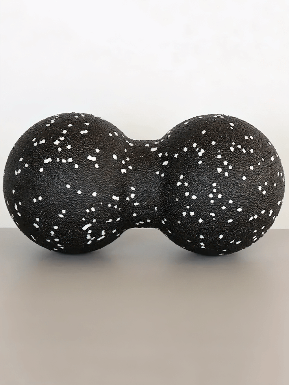 Black double-sided massage ball with white speckles for deep tissue muscle relief and tension reduction.