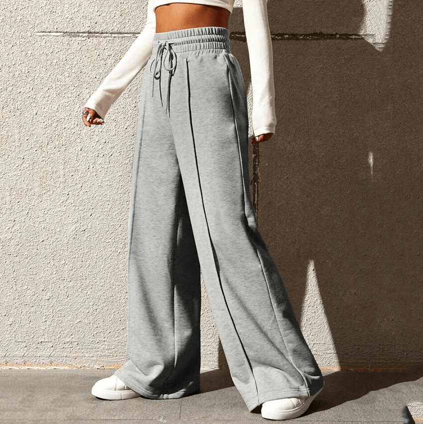 Woman wearing grey drawstring pleated wide leg straight pants with high waist, paired with white top, showcasing stylish and comfy look.