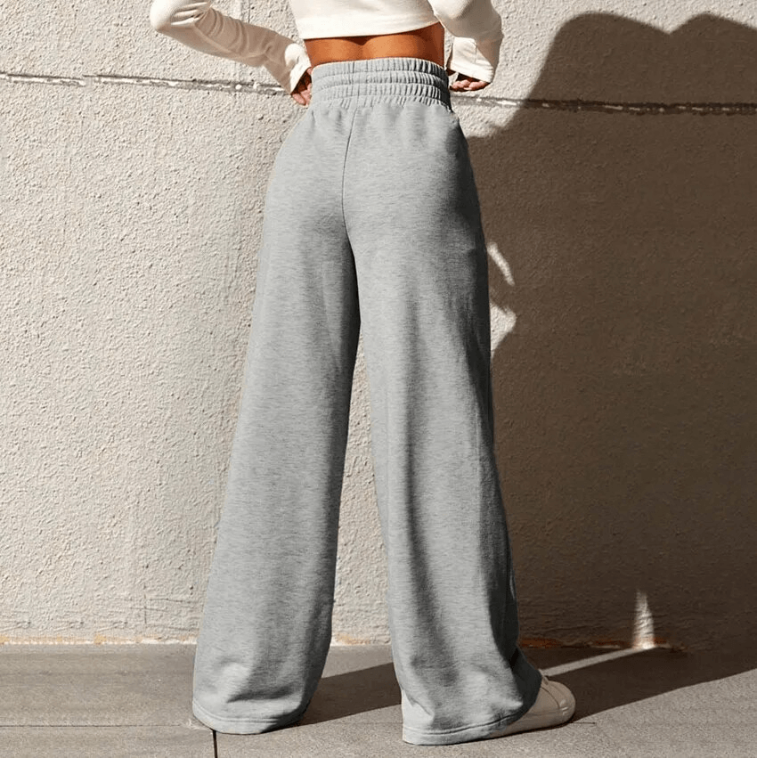 Woman wearing drawstring pleated wide leg pants, high waist design, gray color, showcasing comfortable, stylish fit, against a wall.