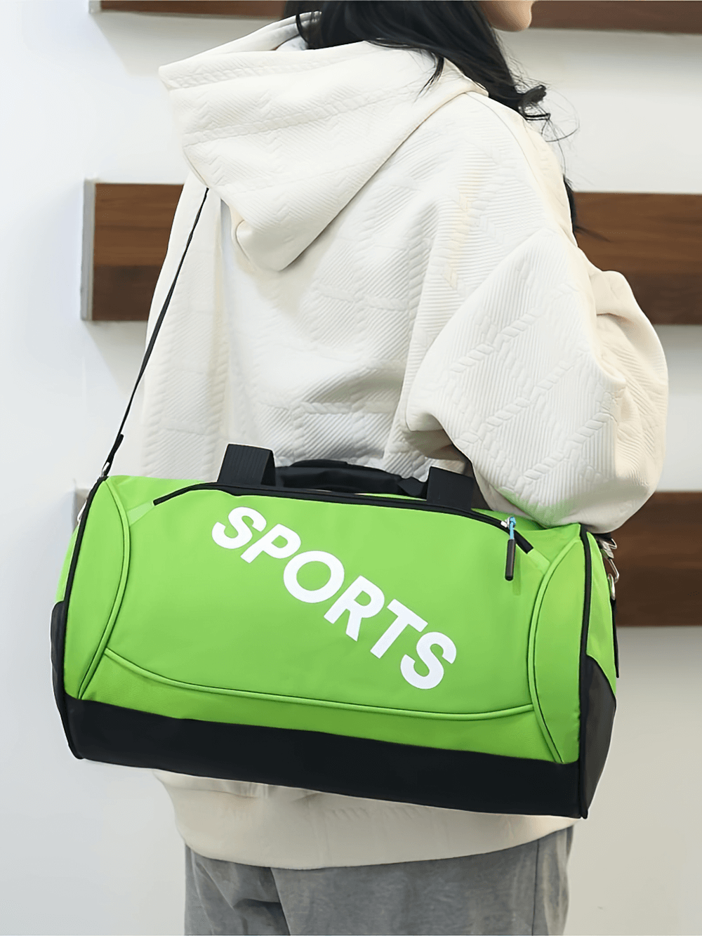 Person carrying green sports duffel bag with 'SPORTS' print, featuring durable Oxford fabric and secure zipper, ideal for gym and travel.