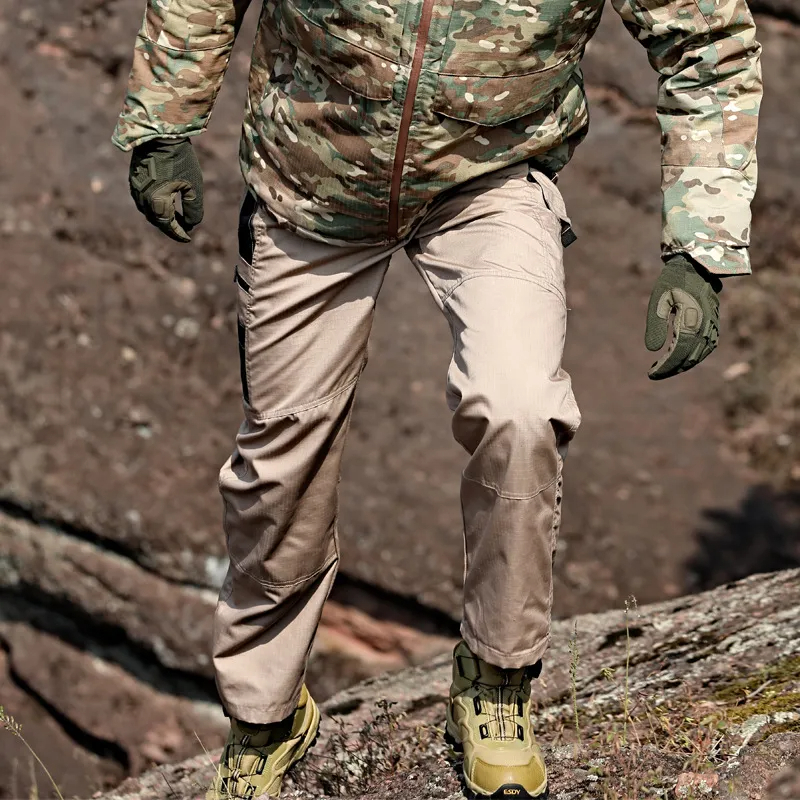 Man climbing rocks wearing durable trekking trousers with pockets, showcasing reinforced knees and tactical design.