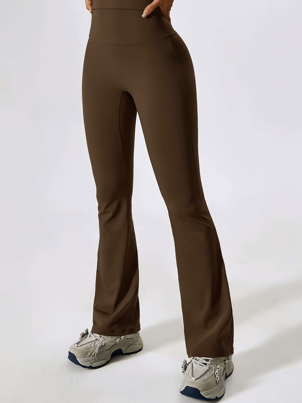 Woman wearing brown flared high-waist yoga pants and sneakers, showcasing wide-leg design and elastic waistband for workouts or yoga.