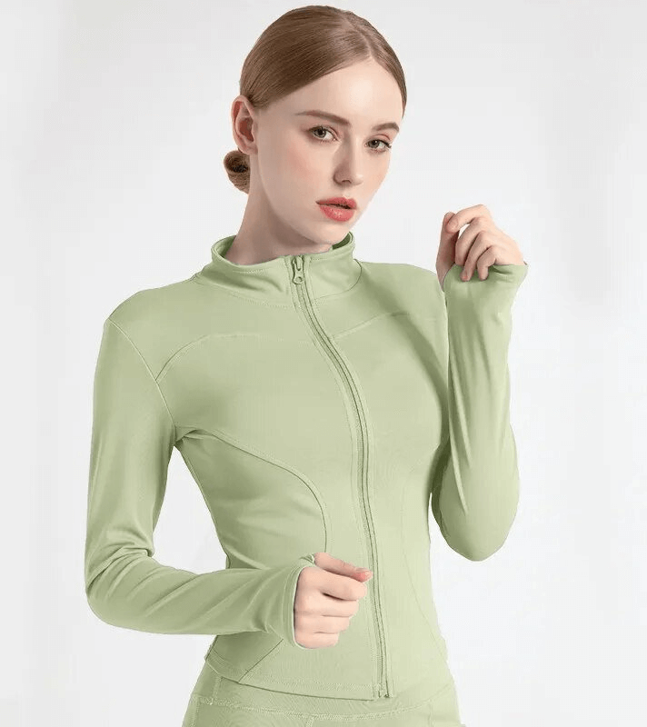 Model wearing a light green elastic sports women's jacket with a zipper and finger holes, perfect for running and exercise.